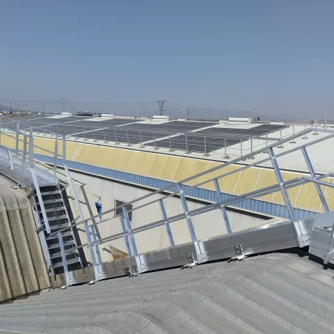 Pasarela con barandillas y sistema anticaídas para mantenimiento seguro en cubierta industrial.
