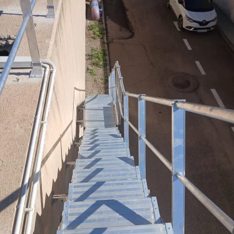 Escalera de mantenimiento con peldaños antideslizantes y barandilla en un lado.