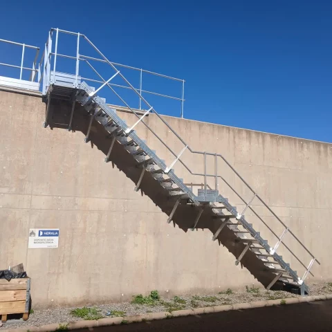 Vista lateral del conjunto: escalera fija con barandilla y plataforma superior de acceso.
